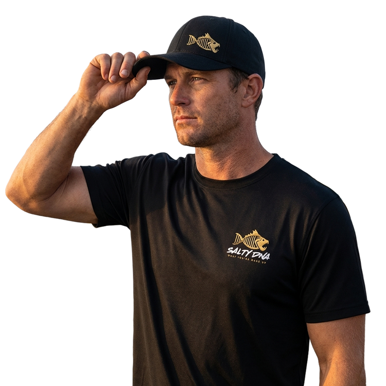 Man wearing a black Salty DNA T-shirt and cap at a marina