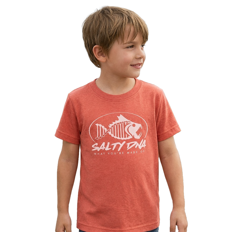 Boy wearing a coral Salty DNA youth T-shirt by the ocean