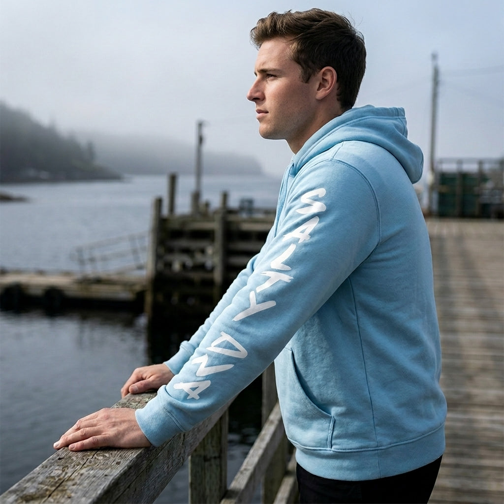 Model wearing a light blue Salty DNA Originals Summer Hoodie with white sleeve lettering by the waterfront