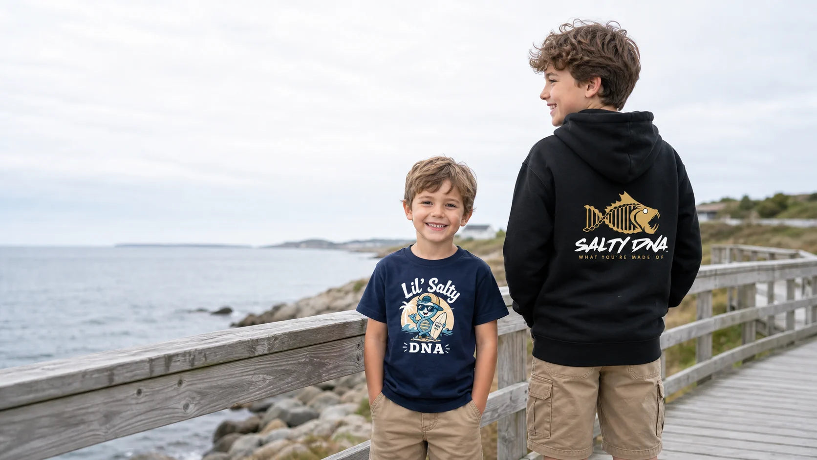 A child and teenager wearing Salty DNA apparel on a coastal boardwalk